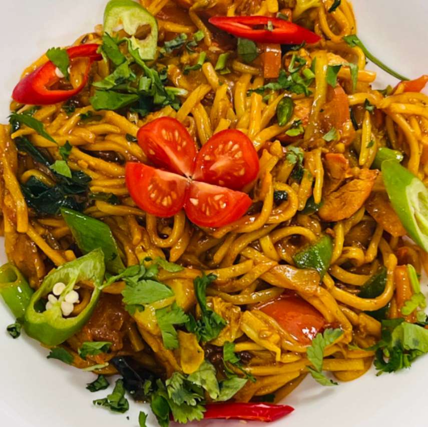 Stir-fried noodles with vegetables, topped with red and green chilies, cilantro, and cherry tomatoes.