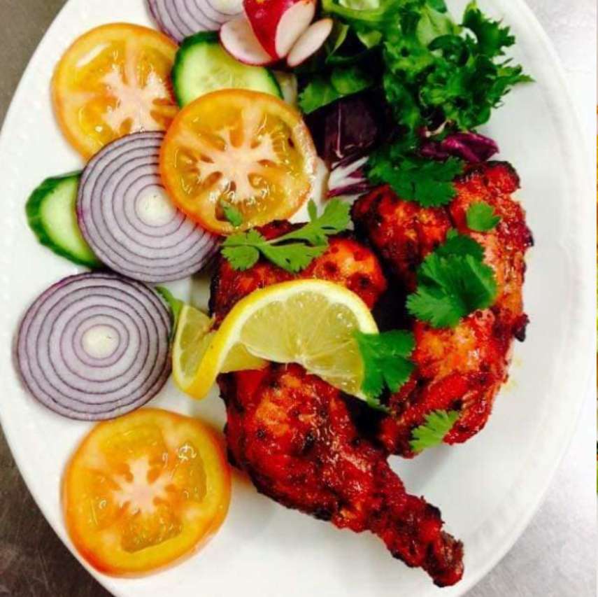 Tandoori chicken served with lemon, cilantro, onions, tomatoes, cucumbers, and a fresh salad.