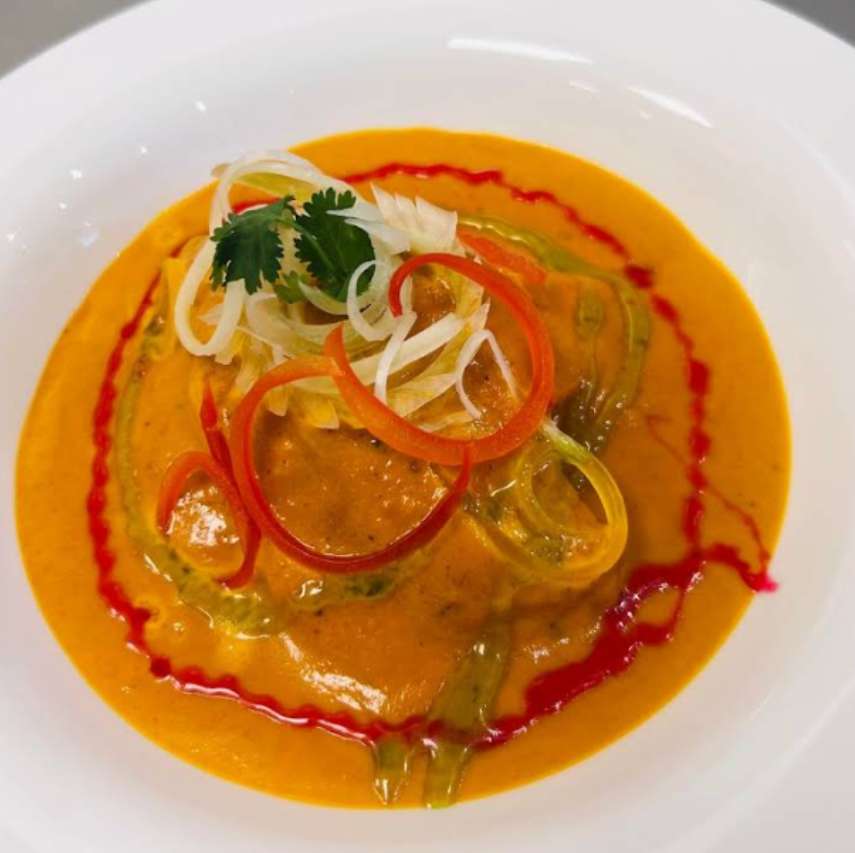 A white bowl filled with orange curry, topped with sliced peppers, onions, and cilantro.